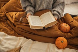 Student reading a book beside pumpkins.